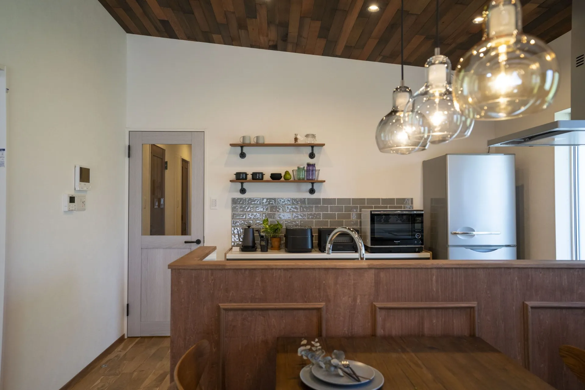 天井にヴィンテージウッドを貼ったキッチンはデザイナー照明でモダンさをMIXさせた。
