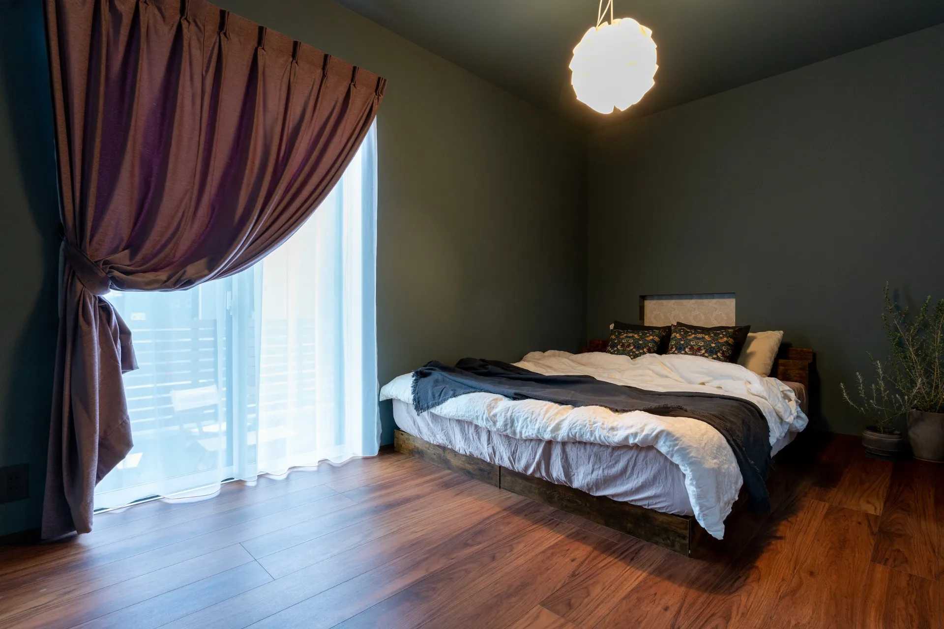 寝室は全体をオリーブカラーの壁紙。カーテンやベッドリネンにスモーキーピンクを採用。かっこよく見えがちなグリーンがピンクで優しくなる効果